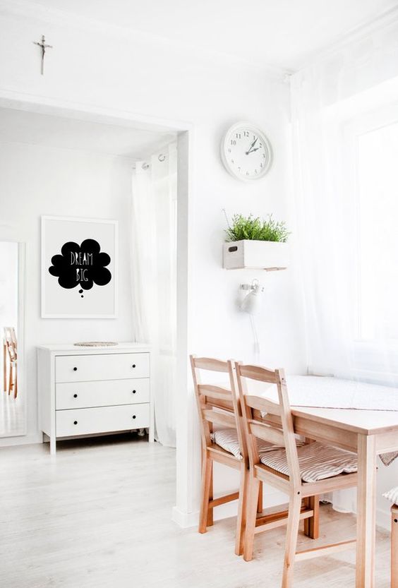 غرفة طعام ذات حيطان بيضاء وكراسي خشبية مع ديكور نباتات داخلية 