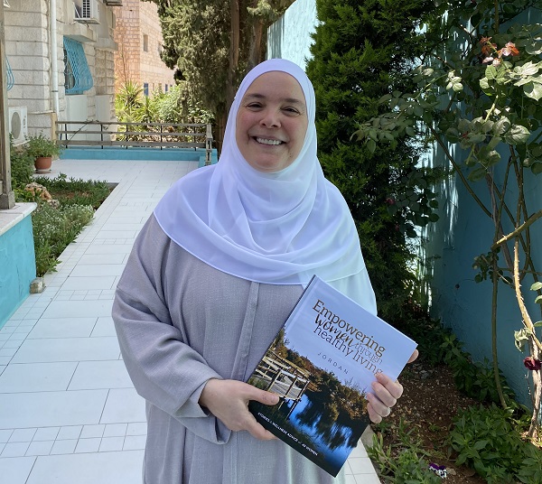 امرأة تبتسم و تحمل كتاب تمكين المرأة من خلال الحياة الصحية في الأردن 