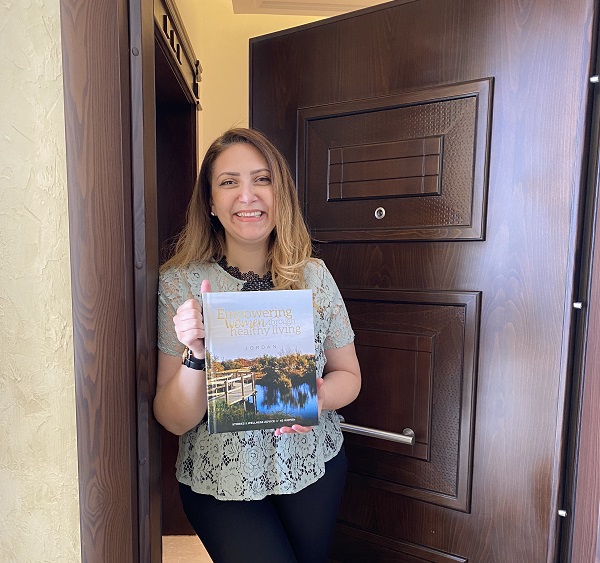 امرأة تبتسم و تحمل كتاب تمكين المرأة من خلال الحياة الصحية في الأردن 