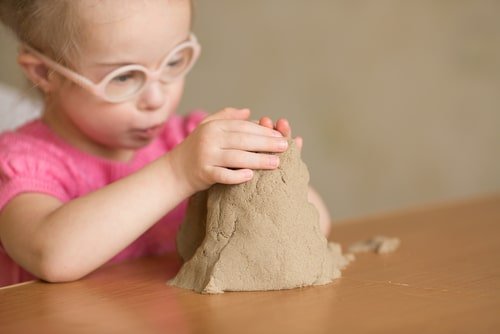 طفلة من ذوي الاحتياجات تلعب بالصلصال والرمل