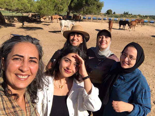 A group of women enjoying their time with horses behind them