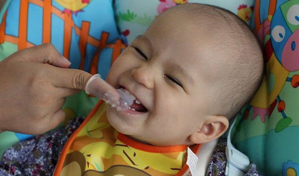  a mom cleaning her kid's tooth with a rubber/silicone finger tooth