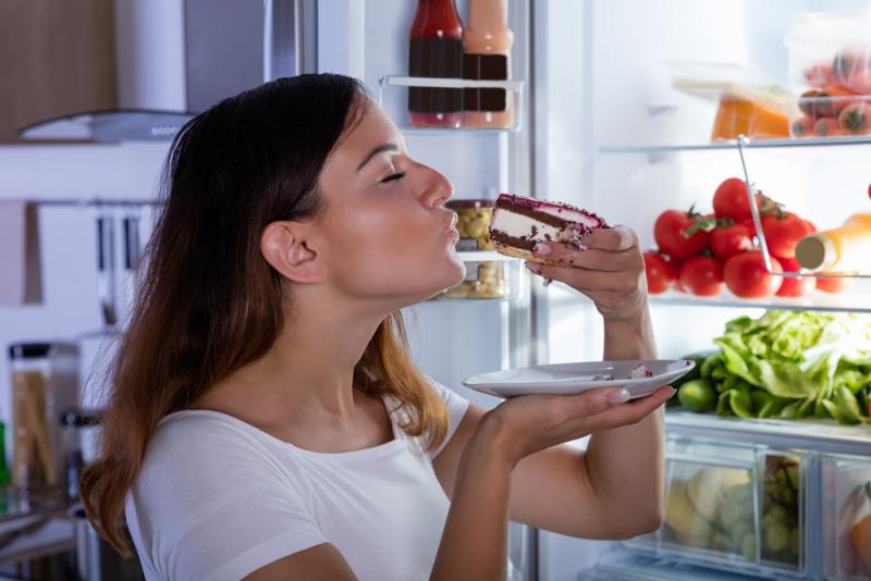 a girl eating a cake from the refrigerator directly 