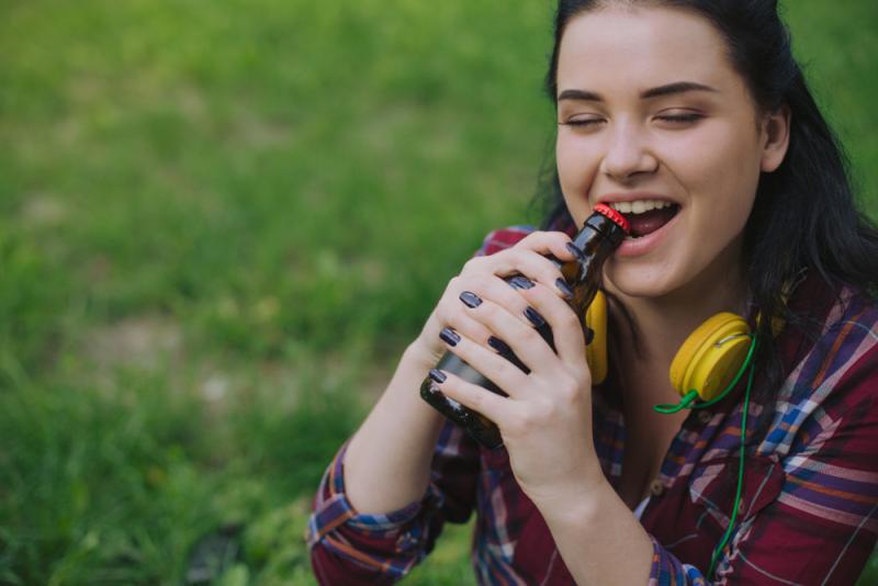 a girl using her teeth to open a drink 