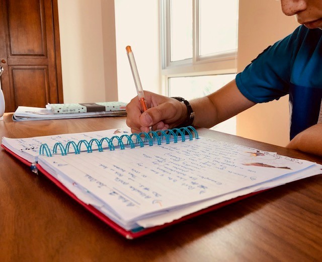 a kid holding a pen and writing in his notebook