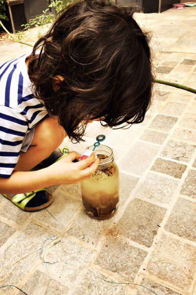 a kid playing outside with a jar filled with water and sand