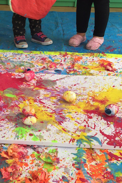 two kids playing with colors and painting on a large peace of paper on the ground