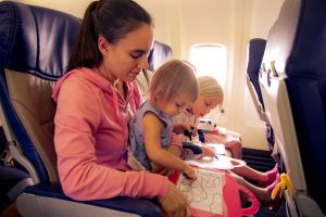 a mom and her little girl setting in an airplane seat and playing with some toys