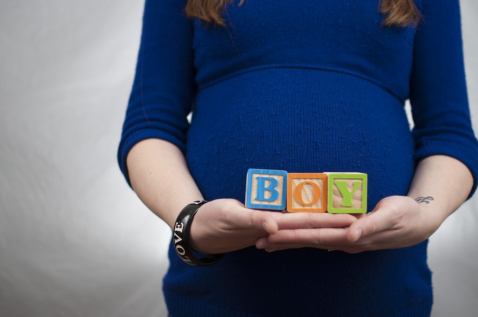 Pregnant mom holding in her hands little boxes that carries the word Boy