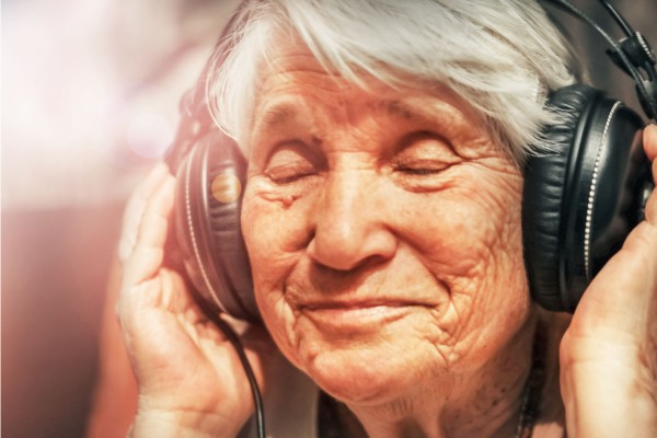 سيدة كبيرة في العمر تضع السماعات على اذانها لسماع الموسيقى ةو تبدو سعيدة 